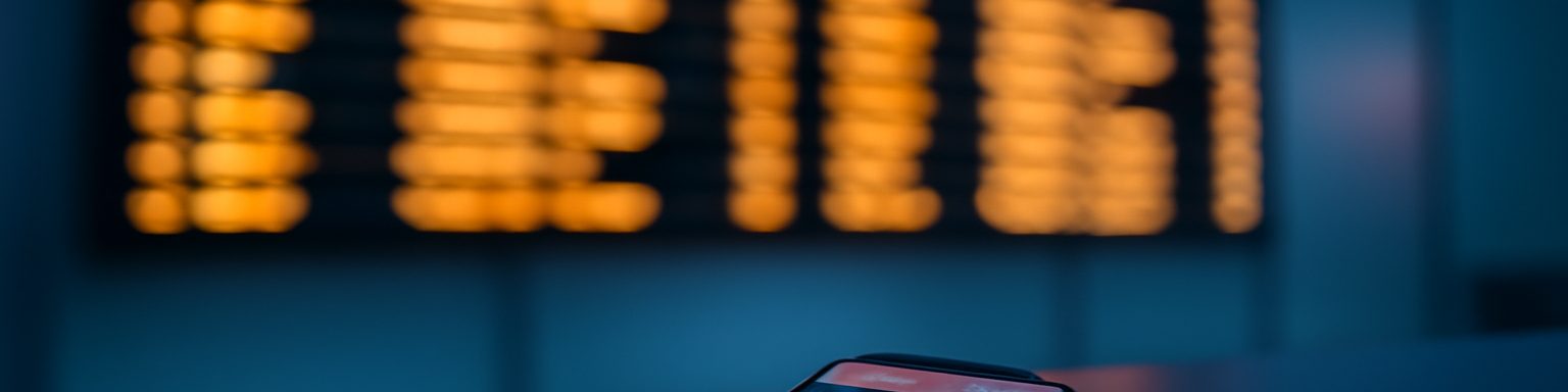 Panel de salidas de un aeropuerto con destinos de varios países junto a un teléfono con una aplicación de apuestas, imagen de esta comparativa de casas de apuestas internacionales